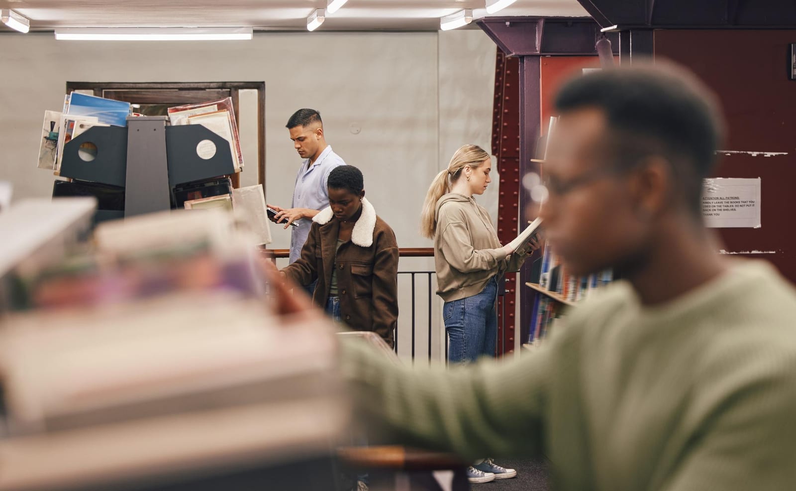 Grupo de pessoas em uma biblioteca, cada uma concentrada em um livro ou em um telefone.